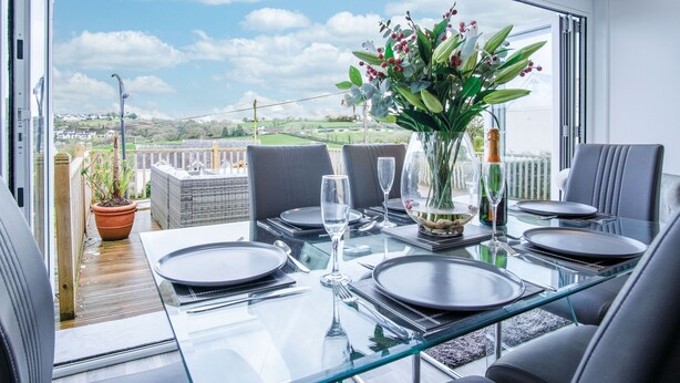 A dining area with a glass table, chairs, and a view of the countryside.