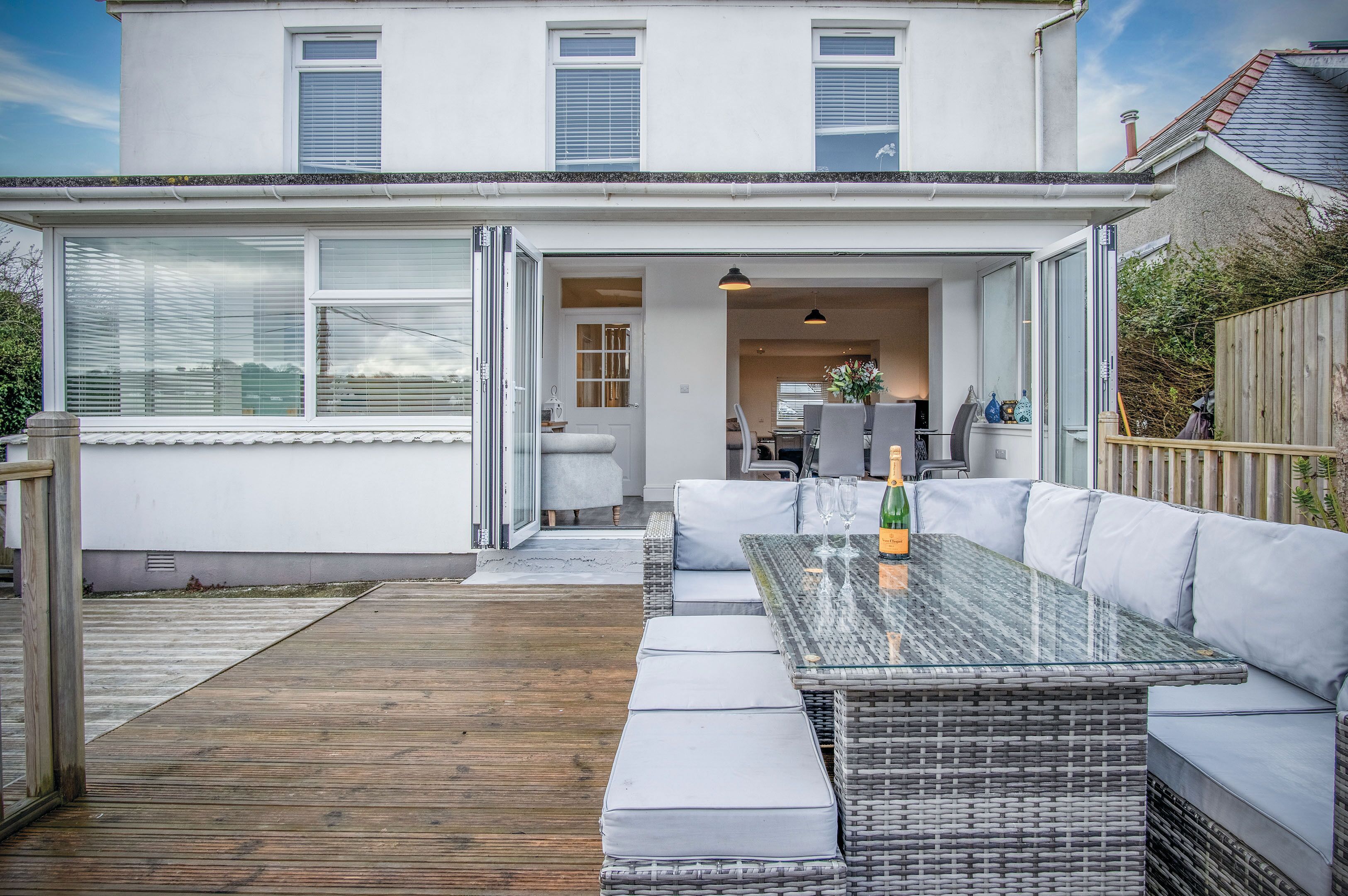 A modern house with a glass-enclosed patio, a glass table with cushions, and a wooden deck.