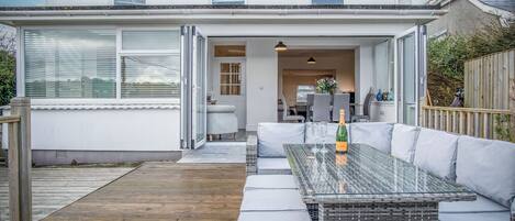 A modern house with a glass-enclosed patio, a glass table with cushions, and a wooden deck.