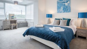 A bedroom with a large bed, bedside lamps, a desk, and a view through the window.