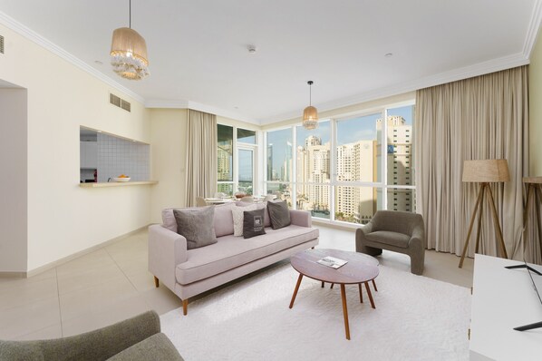 Ein modernes Wohnzimmer mit Sofa, Sessel und Couchtisch, großen Fenstern mit Stadtblick und einer Pendelleuchte.