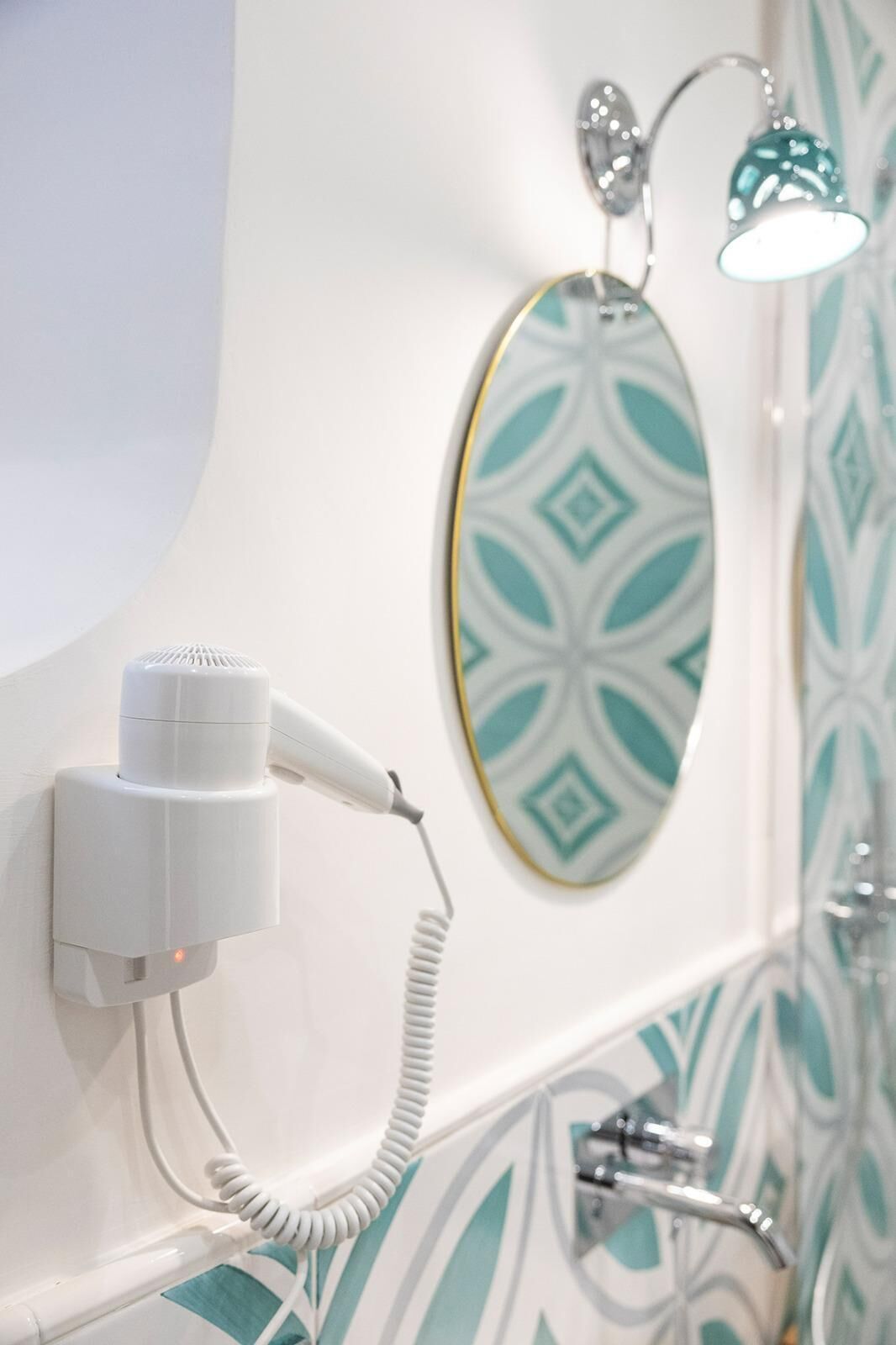Un baño con un secador de pelo montado en la pared, un perchero y un salpicadero de azulejos con diseño.