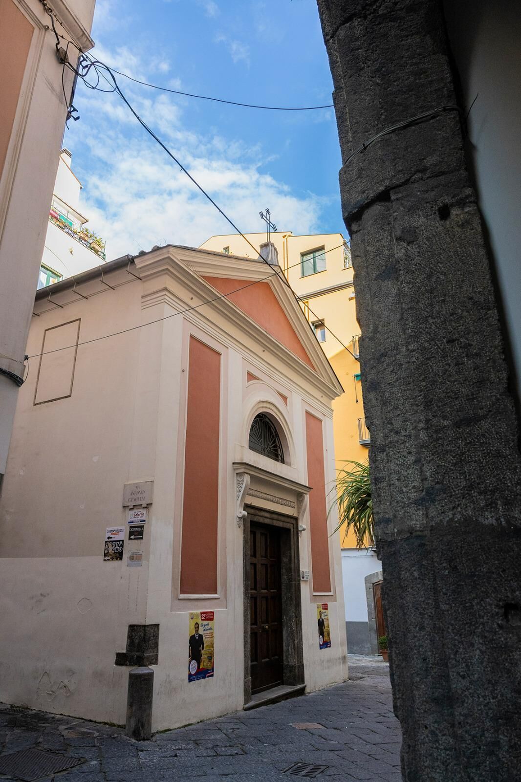 A narrow street with a building featuring a central arched doorway and a small porch.