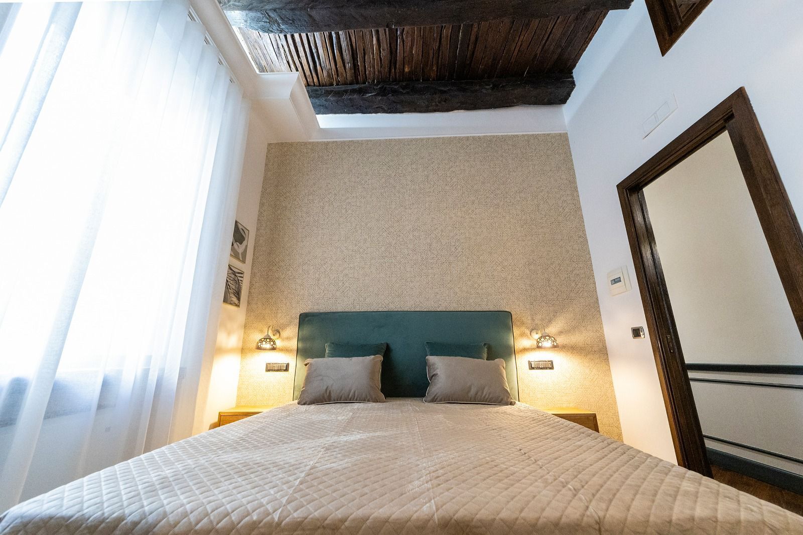 Een slaapkamer met een bed, twee bedlampjes, een houten plafond en een grote spiegel aan de muur.