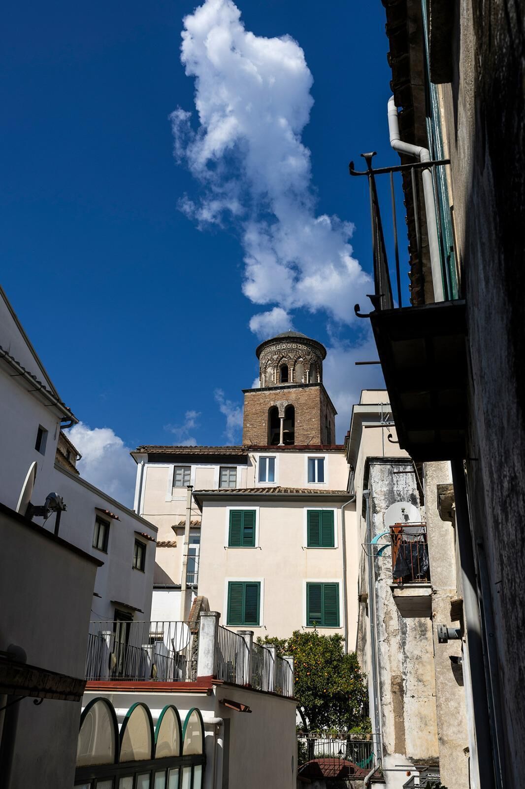 Une rue étroite bordée d’immeubles, une tour surmontée d’un dôme et un ciel d’un bleu limpide.