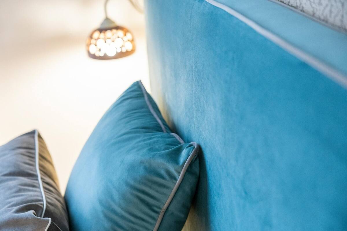 A close-up of a blue upholstered headboard with pillows.