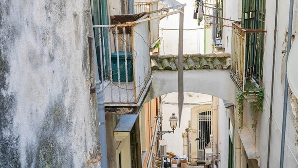 A narrow alleyway with buildings on either side, featuring balconies with plants, a satellite dish, and a staircase. - B&B Boutique Epoca (Salerno)