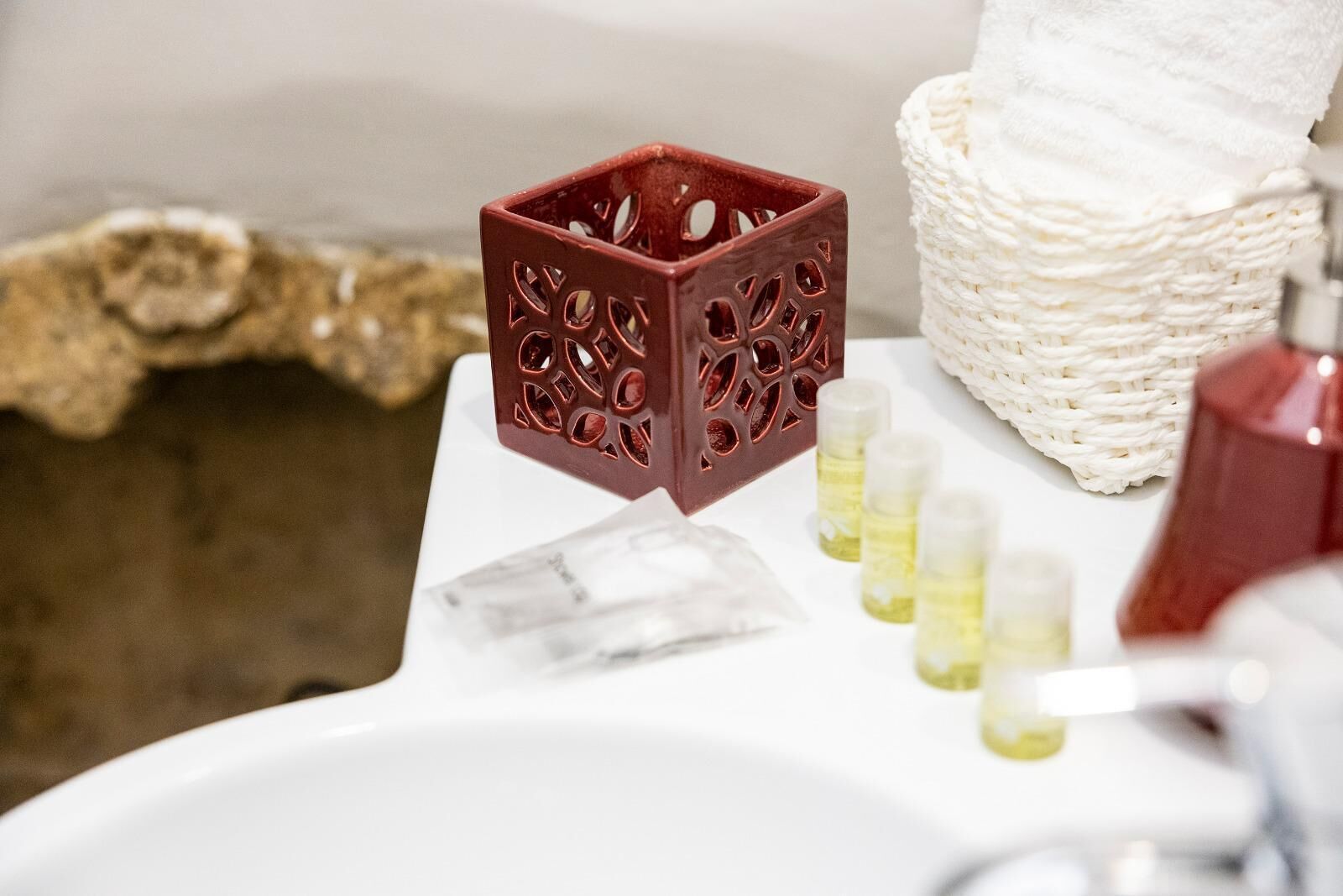 Un baño con un lavamanos blanco, un cubo decorativo rojo y una cesta tejida.