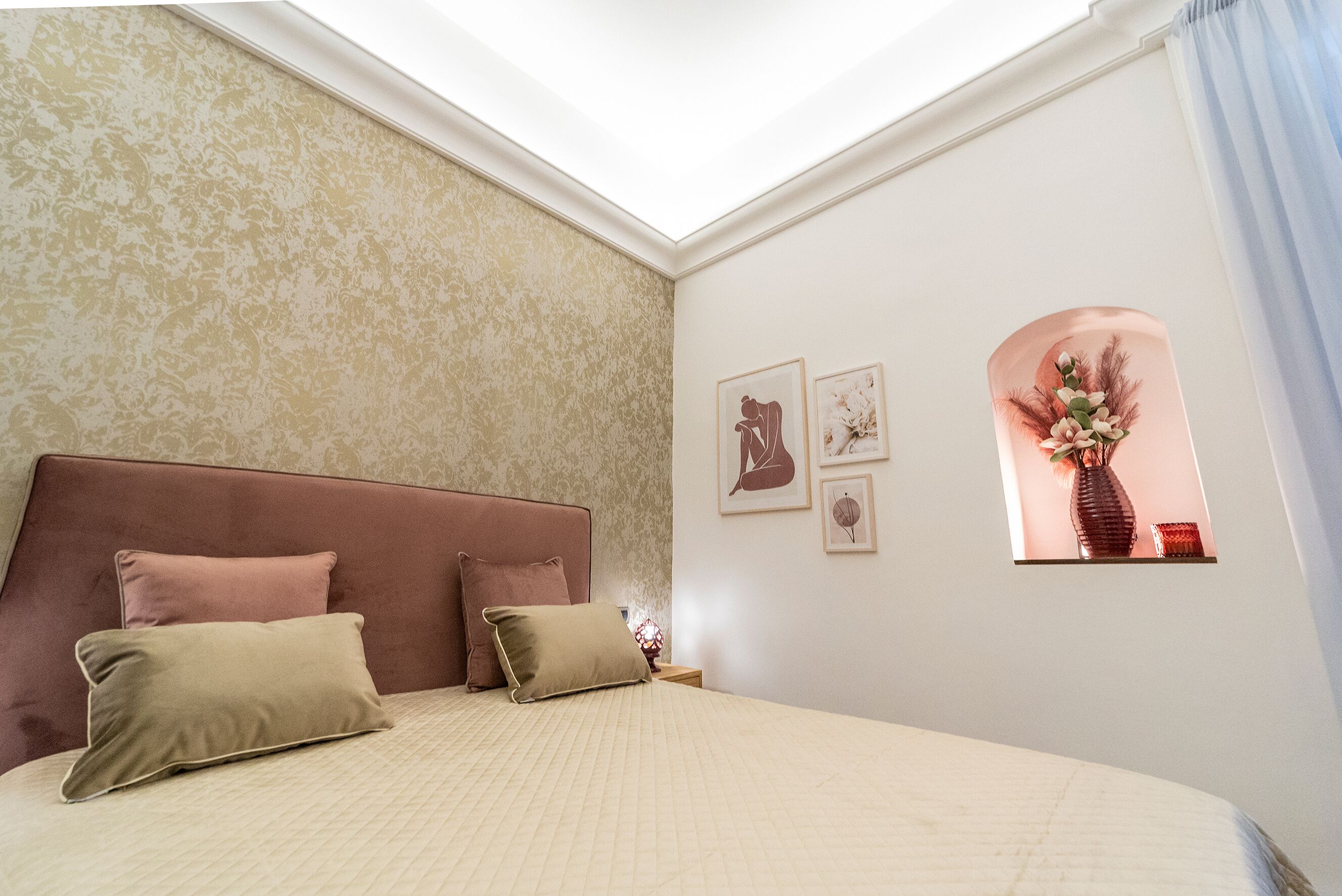 A bedroom with a large bed, a headboard, and a window with a view of a vase and flowers.