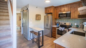A modern kitchen with wooden cabinets, stainless steel appliances, and a marble countertop. - On the River, Downtown Estes Park, Close to RMNP Entrance (Estes Park)