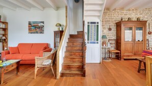 A wooden staircase leading to a door with a green and white patterned window, a wooden cabinet with glass doors, and a red sofa in a room with wooden flooring and white walls. - 700m from the beach, charming house for 5 (Penmarch)