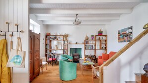 A cozy living room with wooden floors, a green armchair, a wooden staircase, and a bookshelf filled with books and decorative items. - 700m from the beach, charming house for 5 (Penmarch)