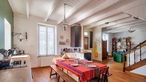 A spacious dining area with a wooden table set for four, a bench, and a kitchen in the background. - 700m from the beach, charming house for 5 (Penmarch)