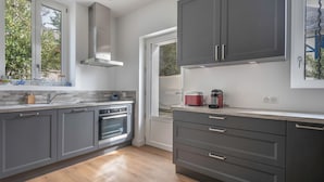 Una cocina moderna con armarios grises, una campana extractora de acero inoxidable y una ventana con vistas a la vegetación.