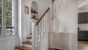 Una escalera con barandillas blancas y peldaños de madera que conduce a un rellano. Se ve un radiador blanco en el rellano.