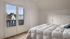 Un dormitorio con una cama grande, paredes blancas y vistas a través de un ventanal corredera.