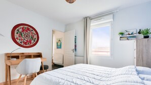 Ein Schlafzimmer mit Bett, Schreibtisch, Stuhl, Heizkörper, Fenster und einer Wand mit einer Dekotasse.
