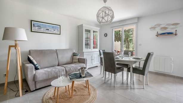 A modern living room with a sofa, coffee table, dining table, and chairs. There is a cabinet with glass doors, a lamp, and a hanging light fixture.