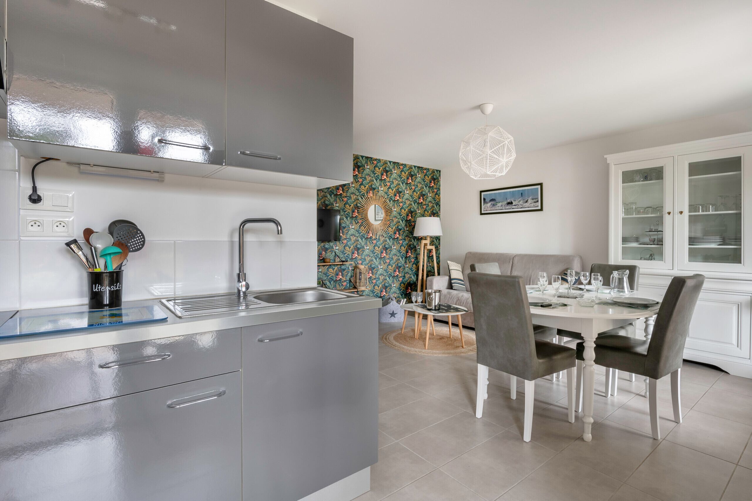 A modern kitchen with grey cabinets, a stainless steel sink, and a dining area with a round table and chairs.