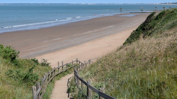 Une plage côtière avec une promenade en bois qui mène au bord de l’eau.