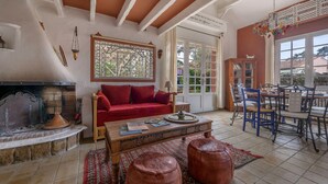 Un salon chaleureux avec une cheminée, un canapé rouge, une table basse en bois et un coin repas avec des chaises bleues.
