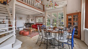 Un vaste espace de vie comprenant une table à manger, des chaises et un canapé rouge. Un escalier avec une rampe en bois mène à l’étage supérieur.