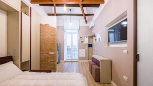 A bedroom with a large bed, a brick wall, and a view of the living area. - Toledo Warm Renovated Studio (Naples)