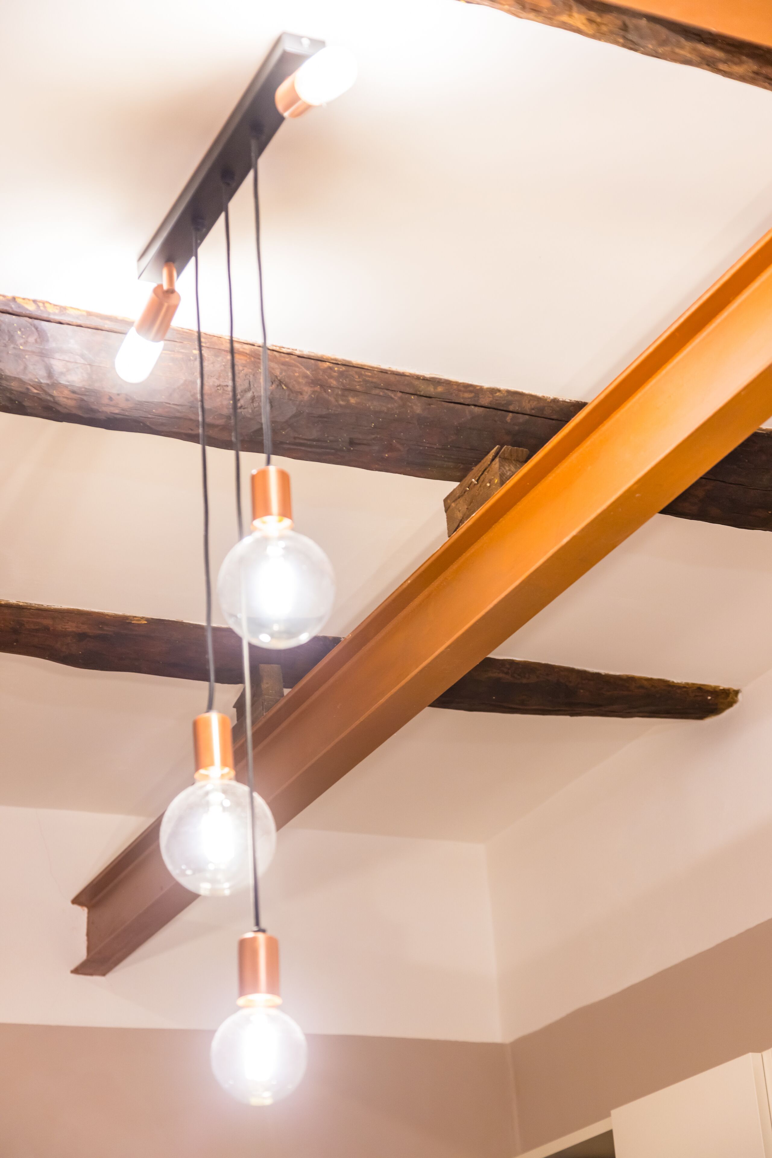 A ceiling with exposed wooden beams and hanging pendant lights with clear glass globes and copper accents.