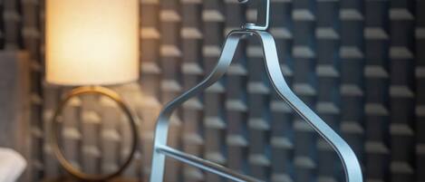 A metal hanger with a hook, a round table with a lamp, and a patterned wall in the background.