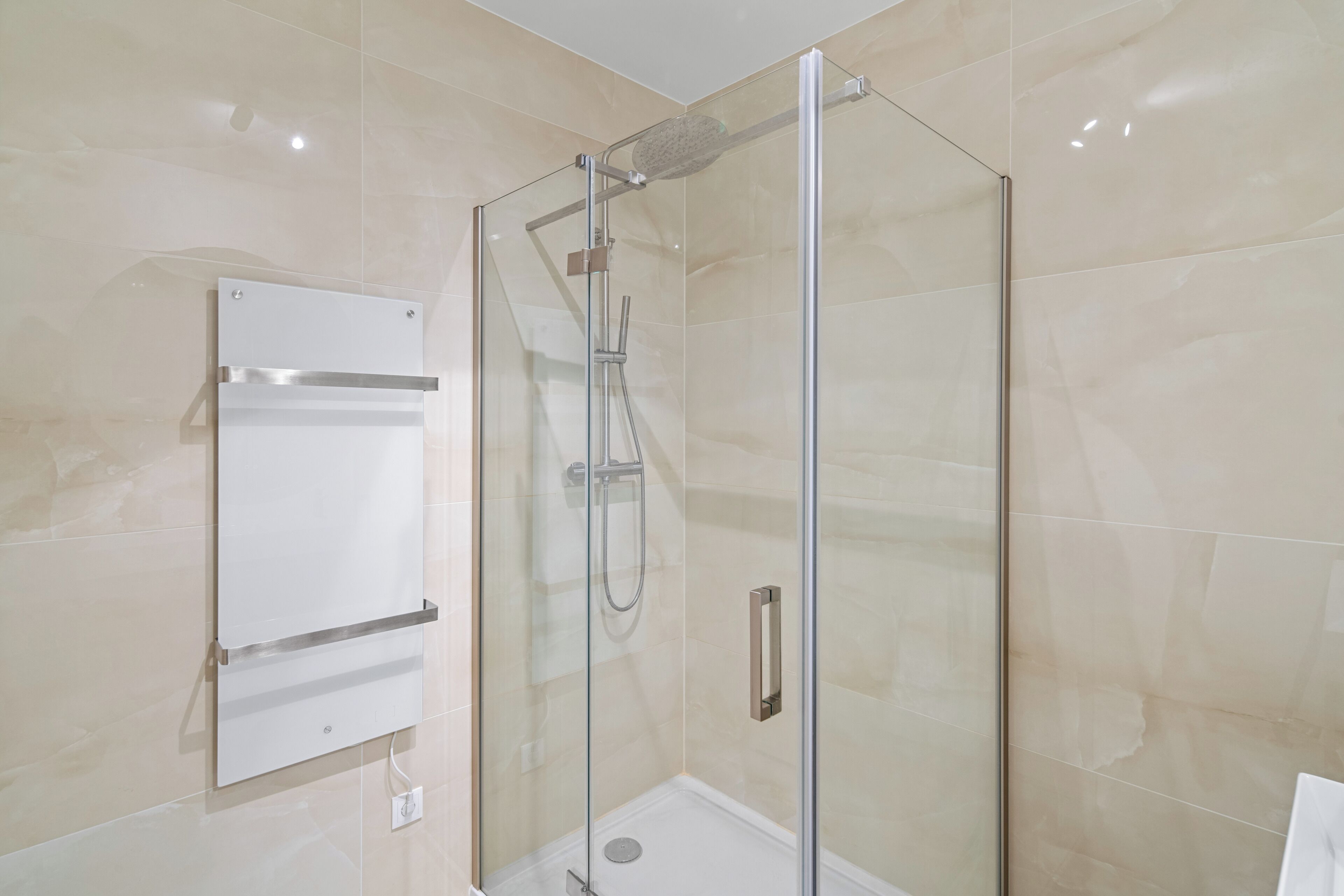 A glass-enclosed shower with a handheld showerhead and a wall-mounted control panel.