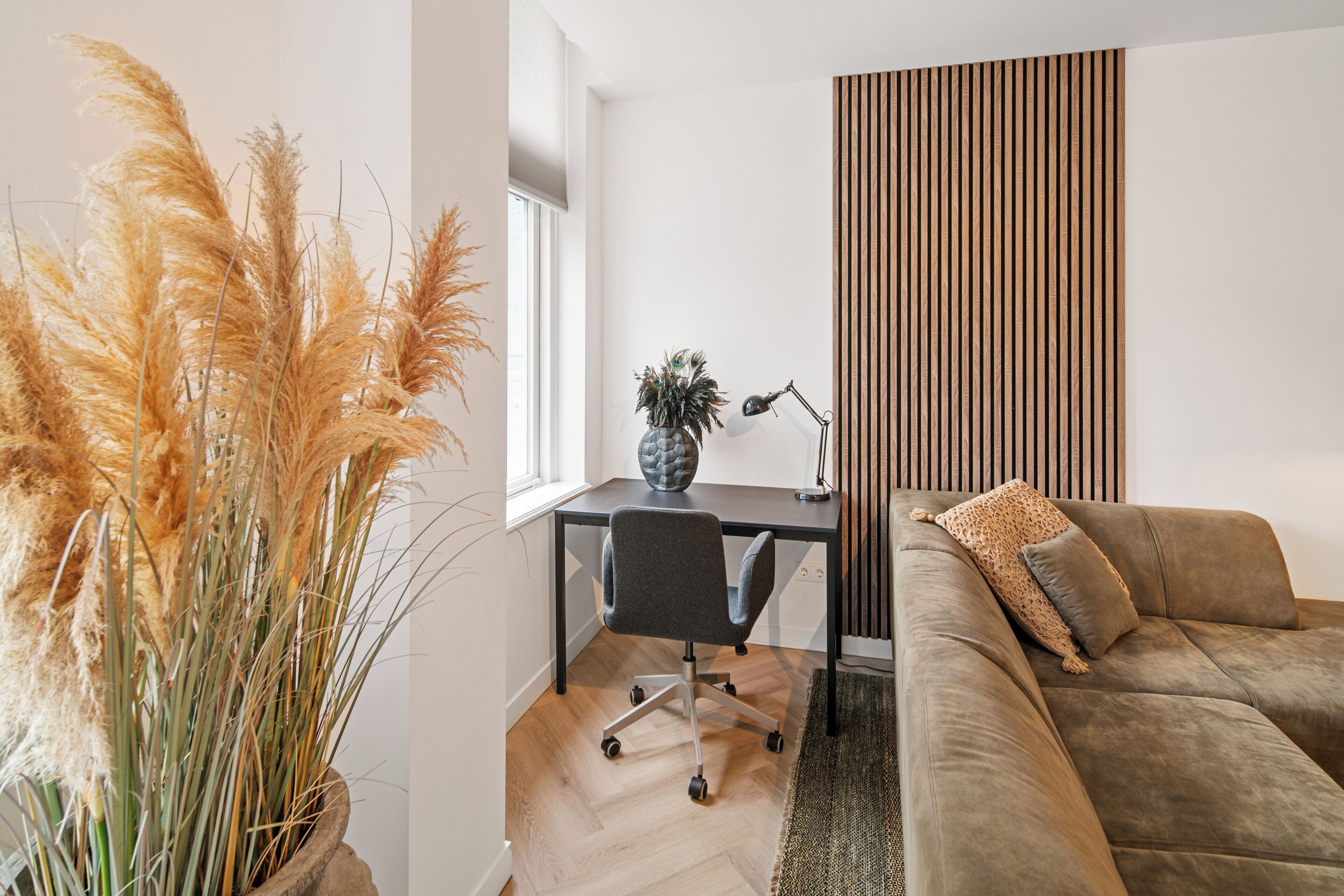Ein modernes Wohnzimmer mit einer Couch, einem Schreibtisch mit Stuhl und einer hohen Pflanze.