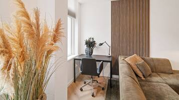 Ein modernes Wohnzimmer mit einer Couch, einem Schreibtisch mit Stuhl und einer hohen Pflanze.