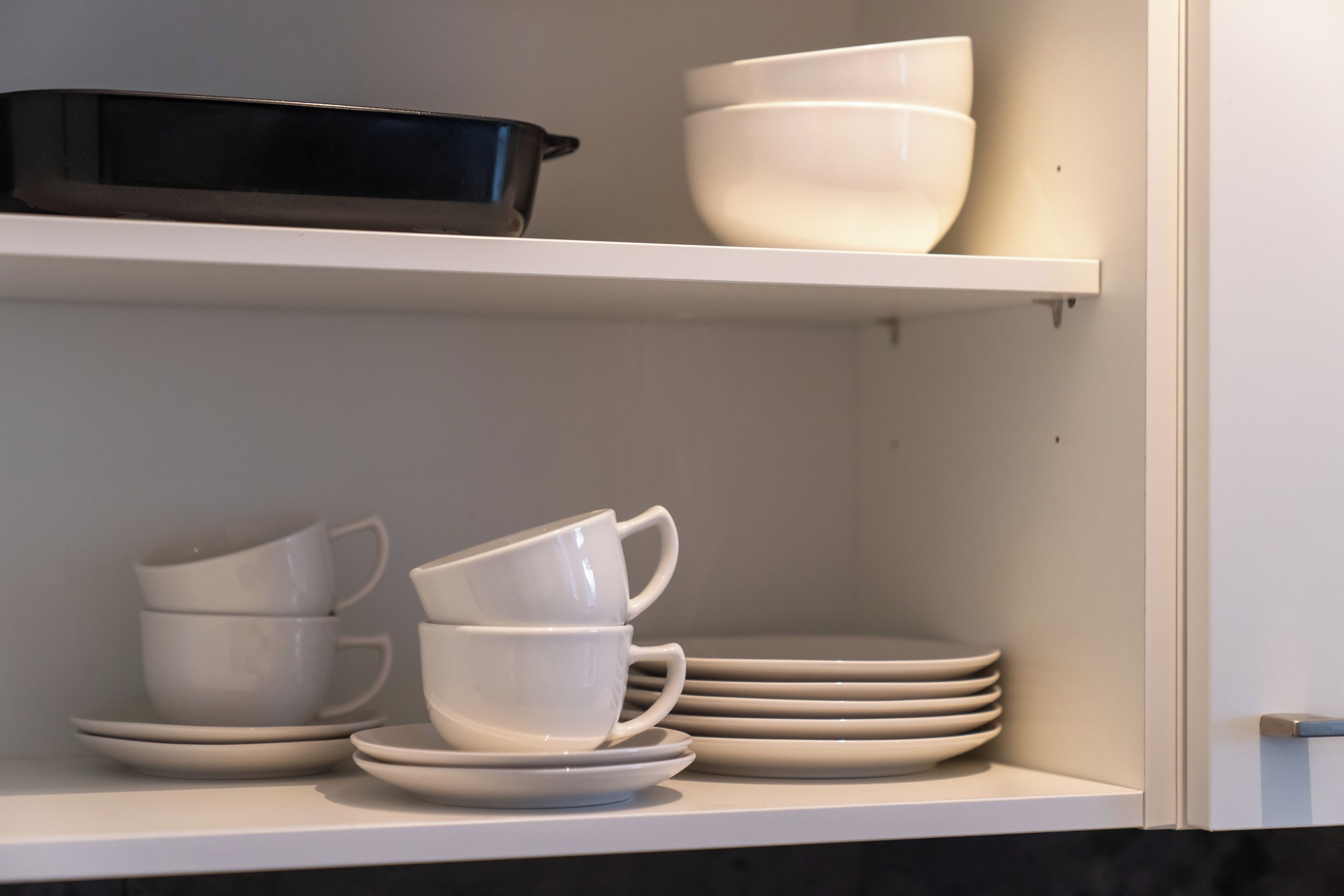A kitchen shelf with white and black cookware, white bowls, and stacked plates.