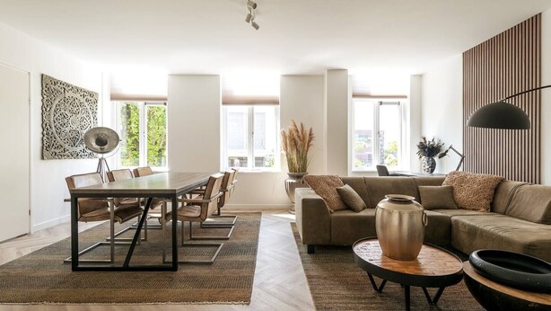 A spacious living room with a dining area, large windows, and a modern design. - Fully equipped for business trips or cozy meals. (Roosendaal)