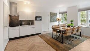 A modern kitchen with white cabinets, a herringbone wood floor, and a dining area with a wooden table and chairs. - Fully equipped for business trips or cozy meals. (Roosendaal)