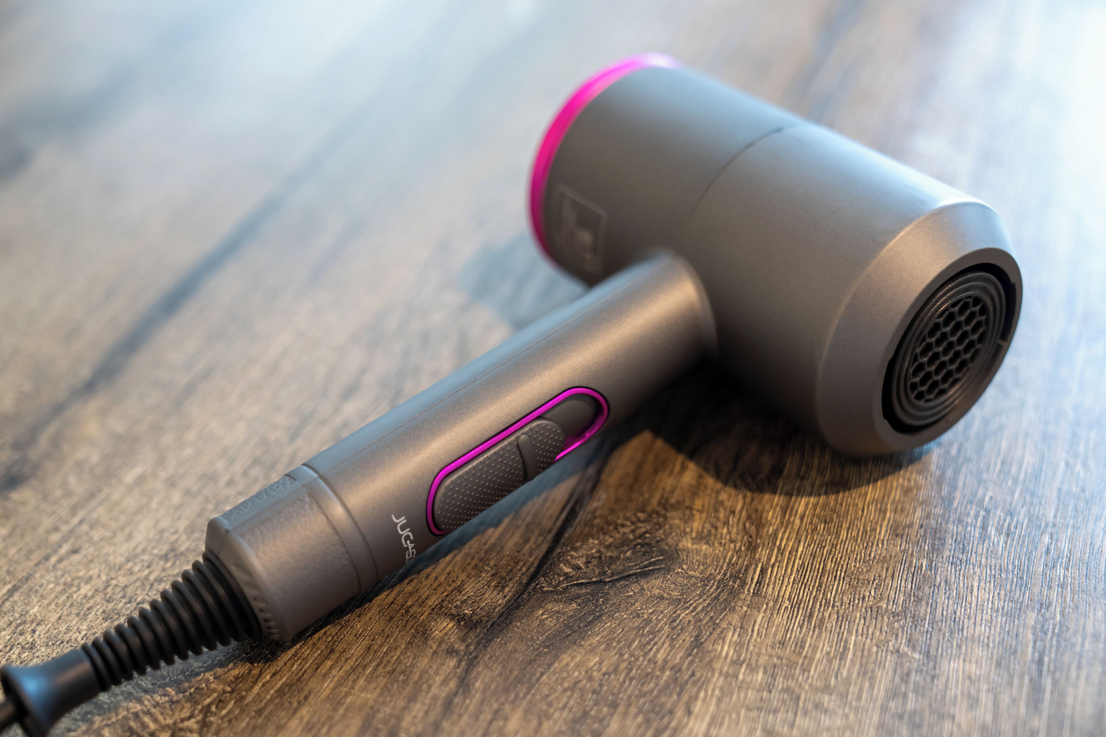 A cylindrical hair dryer with a metallic finish and a pink accent on the top, placed on a wooden surface.
