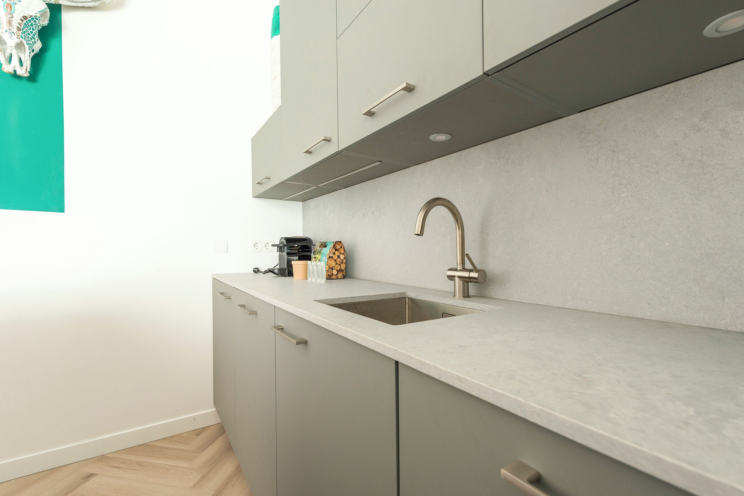 A modern kitchen with a single sink, grey cabinets, and a herringbone-patterned wooden floor.