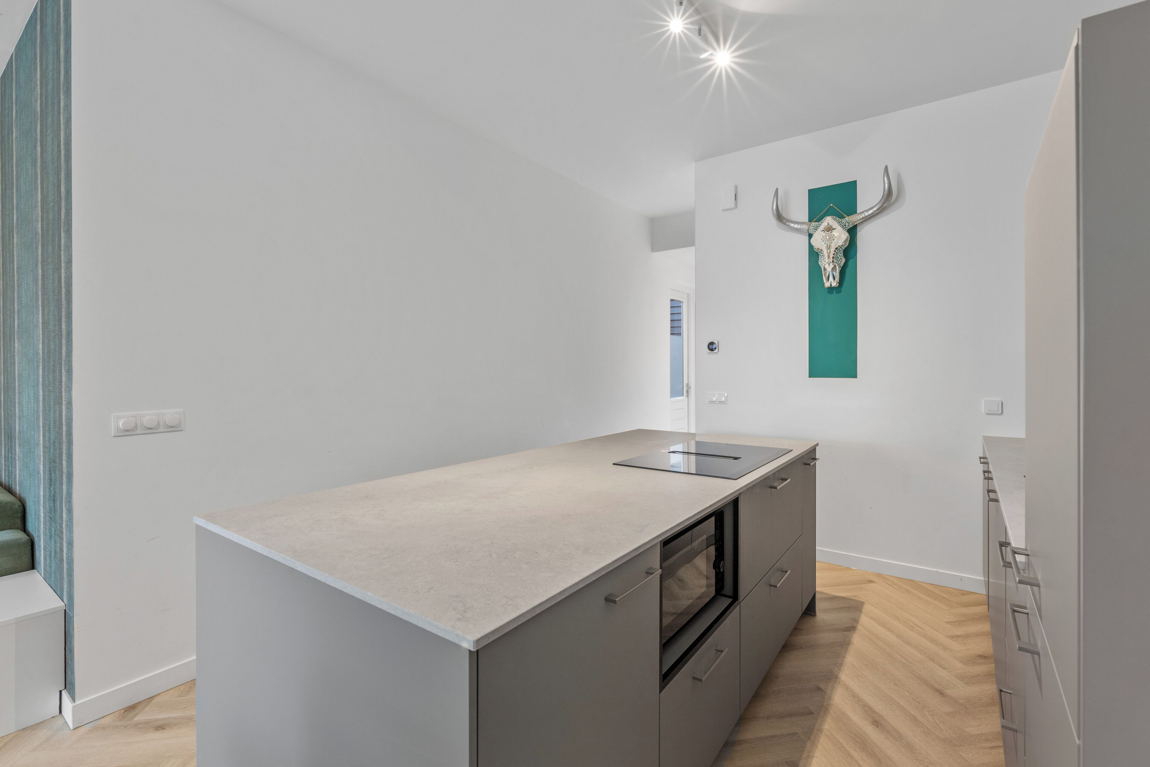 Een moderne keuken met een groot eiland, een ingebouwde oven en een turquoise wanddecoratie.
