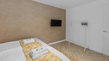 Et moderne hotelværelse med en trævæg, et fladskærms-tv monteret over sengen, et hvidt klædeskab og et håndklædestativ.