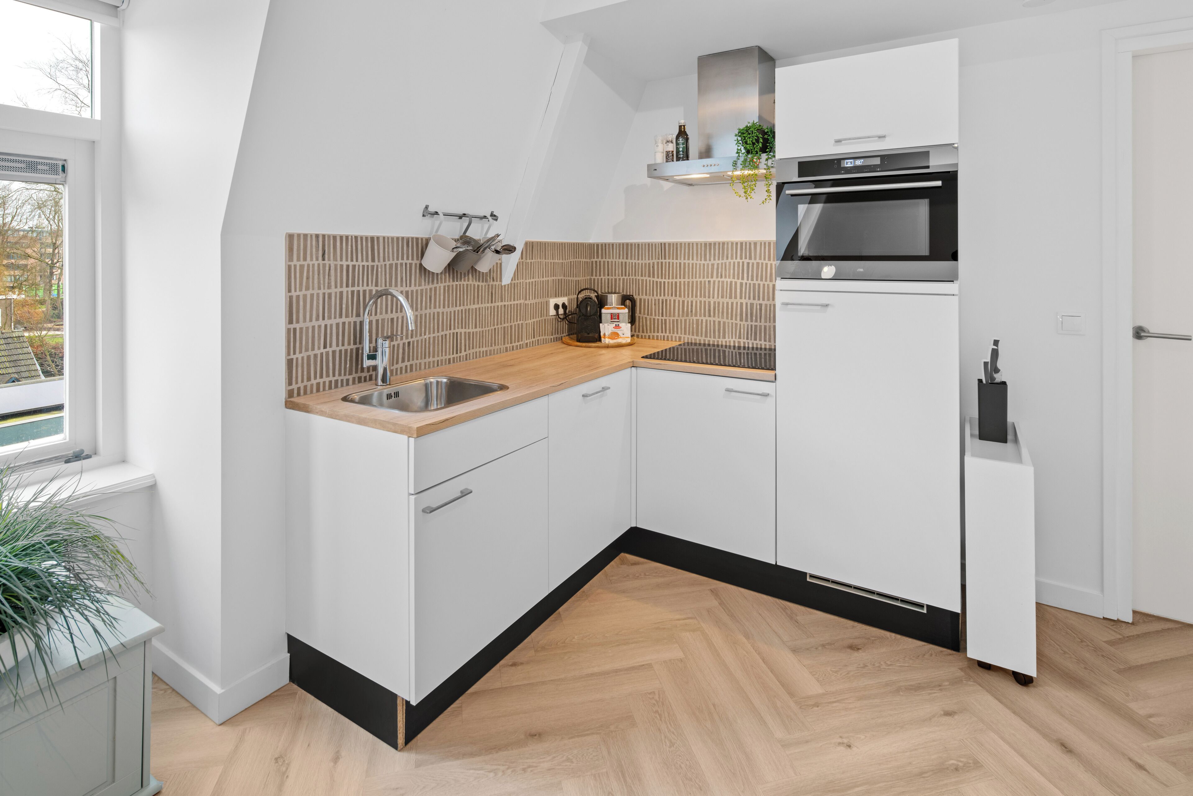 A modern kitchen with white cabinetry, a wooden countertop, a stainless steel sink, and a built-in oven.