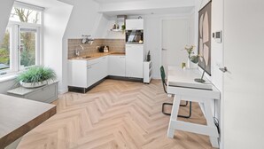 A modern kitchen with white cabinetry, a herringbone wood floor, and a dining area with a white table and chairs.
