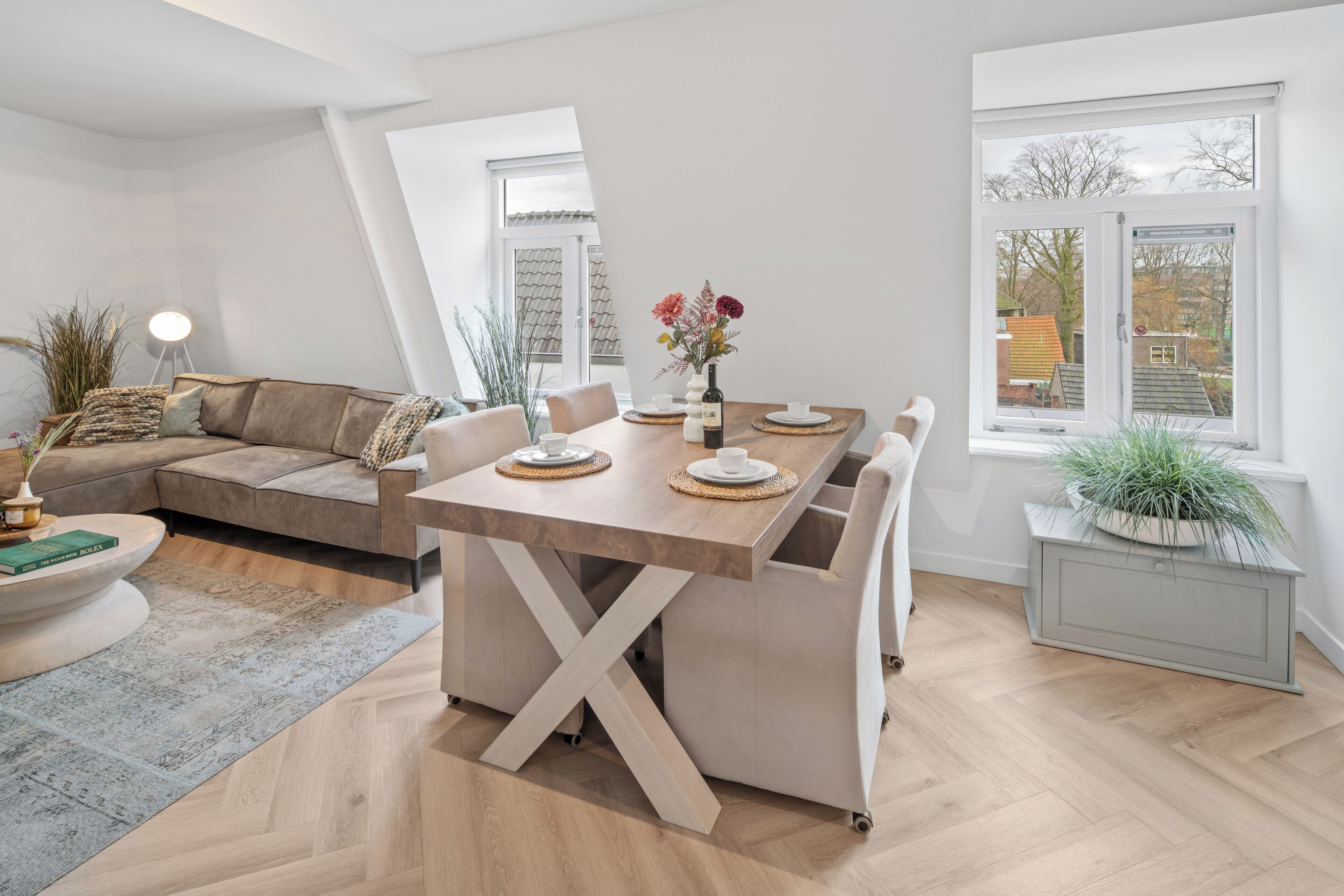 Un salon moderne avec une table à manger en bois, un canapé et une petite table d’appoint sur laquelle est posé un vase de fleurs.