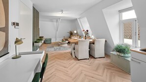 A modern loft apartment with a dining area, kitchen, and a large window providing natural light.