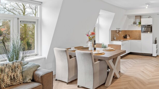 A modern kitchen with white cabinets, a wooden dining table, and a built-in oven.