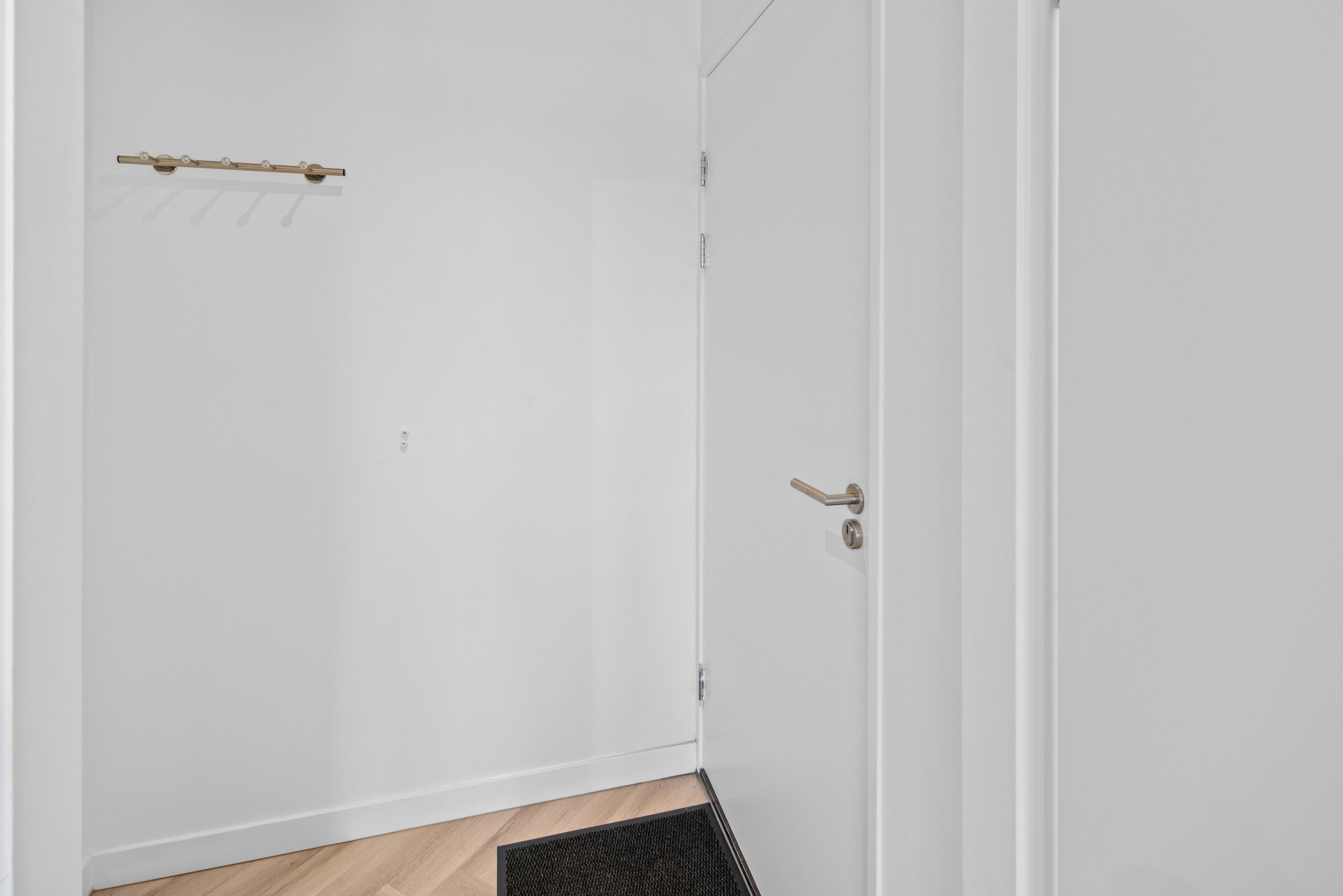 Una porta bianca con maniglia in legno e un bastone di metallo fissato al muro.