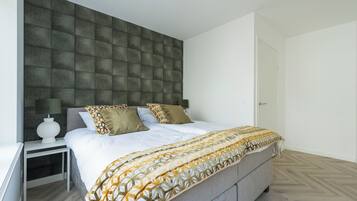 Een moderne slaapkamer met een groot bed, een nachtkastje, een hoofdbord bevestigd aan de muur, en een deur.