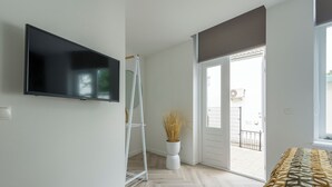 Une chambre moderne avec un téléviseur à écran plat fixé au mur, un lampadaire blanc, une plante en pot et une couvre-lit à motifs.