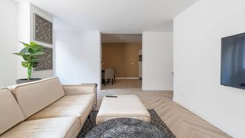 A modern living room with a beige sofa, a patterned ottoman, and a potted plant.