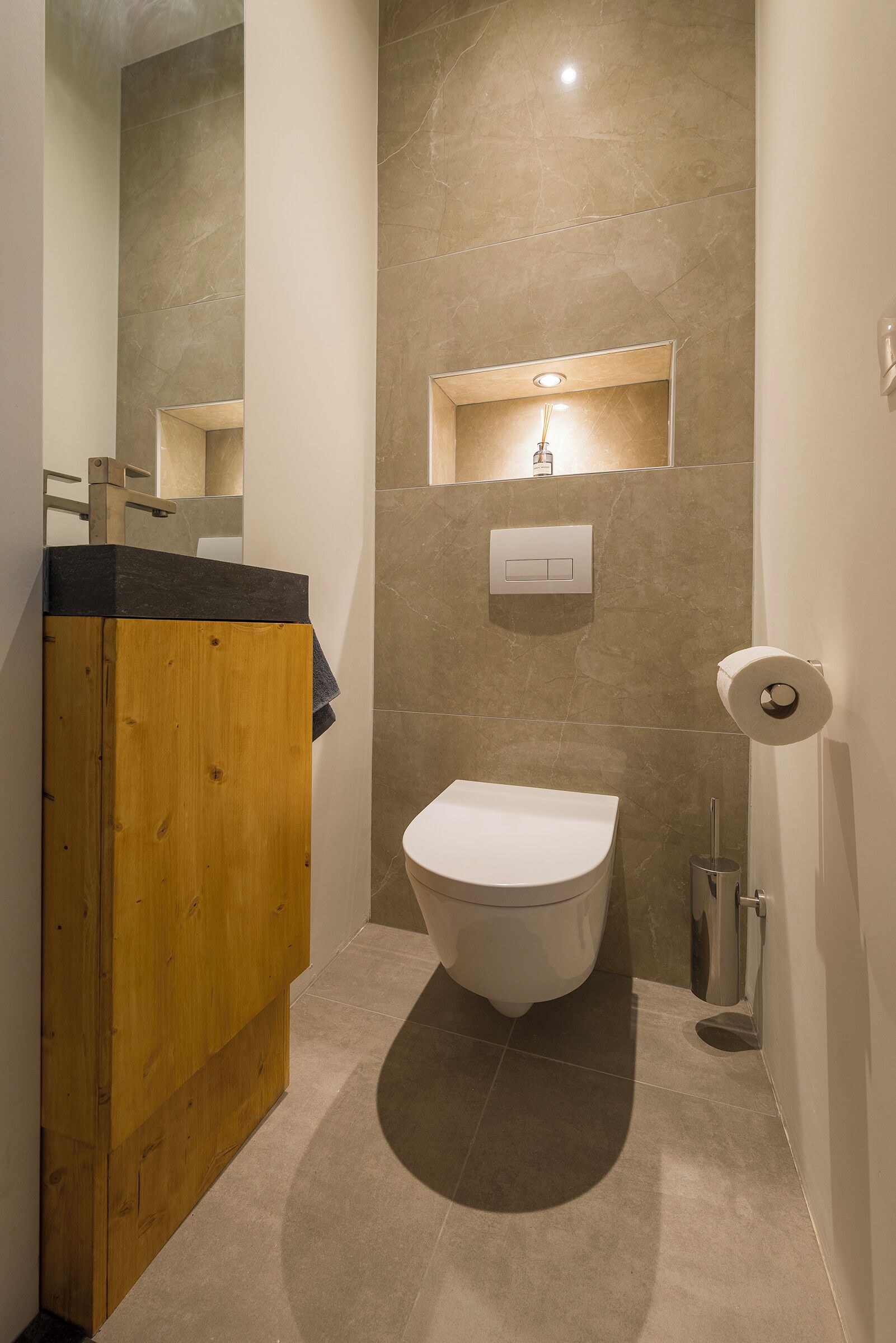 A modern bathroom with a wooden vanity, a white toilet, and a wall-mounted light fixture.