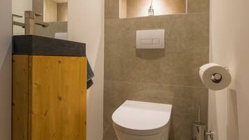 A modern bathroom with a wooden vanity, a white toilet, and a wall-mounted light fixture.